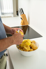 Male hands peeling potatoes in kitchen, preparing fresh homemade meal for family. Healthy cooking,...
