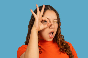 Young woman winking making okay hand gesture
