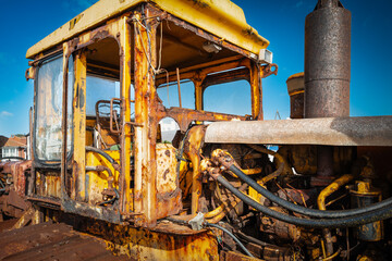 Fototapeta premium Dilapidated and abandoned yellow painted construction excavator showing its heavily oiled engine bay and broken glass on the cabin window. Located at a beach in Britain.