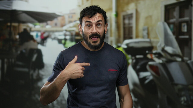 Hispanic man outdoors on a street signals gratitude with expression of thanks and beard, against a background of bustling urban scene with motorbike and people.