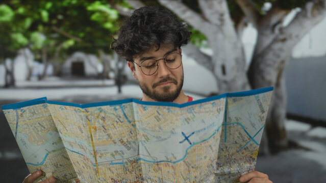 Young man with beard studying map outdoors on a tree-lined street suggesting travel exploration and navigation