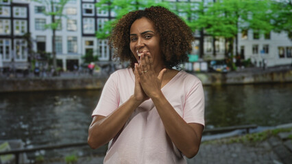 Fototapeta premium Woman clapping hands and smiling with teeth by canal on street in amsterdam, raising fists and applauding in daylight; spontaneous joy celebration.