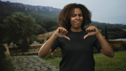Young african american woman giving two thumbs down with hands visible in a forest clearing,...