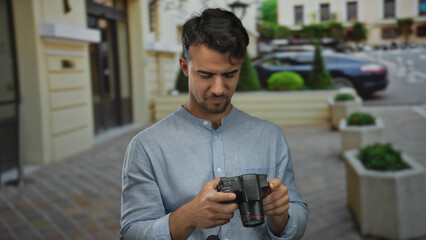 Young hispanic man with camera navigates city street capturing urban scenery, reflecting concentration and creativity in an outdoor setting.