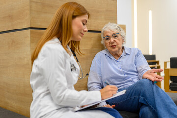 Obraz premium Senior woman explaining medical concerns with female doctor writing on clipboard during hospital checkup