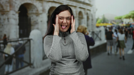 Woman smiling with glasses in front of the coliseum in rome surrounded by people and ancient architecture on a sunny day, showcasing joyful travel vibes.