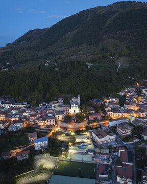 Aerial view of the town nestled against a dark mountain, lights glowing warmly against the deepening twilight, Santo Stefano del Sole, Irpinia, Campania, Italy.