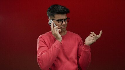 Fototapeta premium Man in glasses with phone against red background displaying expression of curiosity and wonder.