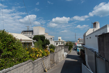 遠くに海の見える晴れて緩やかな坂の路上に建物の影が出来た田舎の路地裏の道