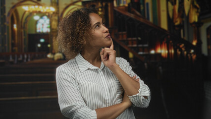 Woman with hand on chin and index finger resting on cheek, arms crossed in church nave gazing...