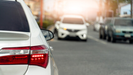 Rear side of luxury white car with turn on brake light. Opposite of road with other cars stop in the junction. Environment in the city at day time.