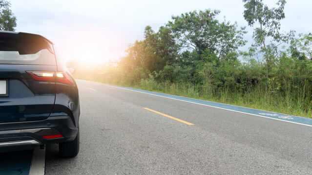 Rear side of dark luxury car with turn on right signal on the asphalt road. Turn on the signal to request to drive in the normal lane. With bicycle lane and side of raod with green grass and trees.