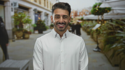 Fototapeta premium Hispanic man smiles showing teeth while wearing a white shirt and standing on a paved city street; optimism wellbeing.