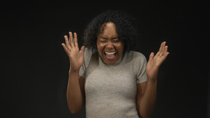 African american woman clenches fists with raised arms in studio against black backdrop;...