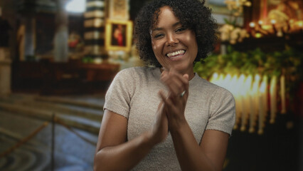 Woman smiling and clapping hands in church aisle under golden candlelight near wooden pews; worship...