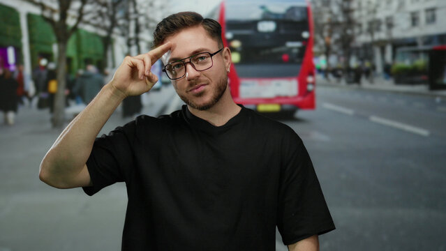 Young man with beard making a salute gesture on a busy city street with a red bus in the background, capturing urban outdoor life.