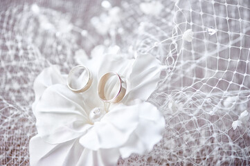 Close-up of two golden wedding rings displayed on a silk flower, surrounded by delicate lace and soft textures. Image evokes romance, love, and the joyful celebration of marriage and commitment.