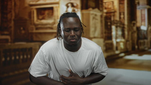 Man clutching chest inside ornate church building, hands pressed to sternum in prayerful pose; pain faith.