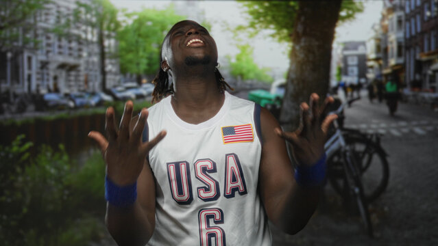 Man in usa basketball jersey with clenched fists and head tilted back looking up on a street; joy celebration victory. - Powered by Adobe