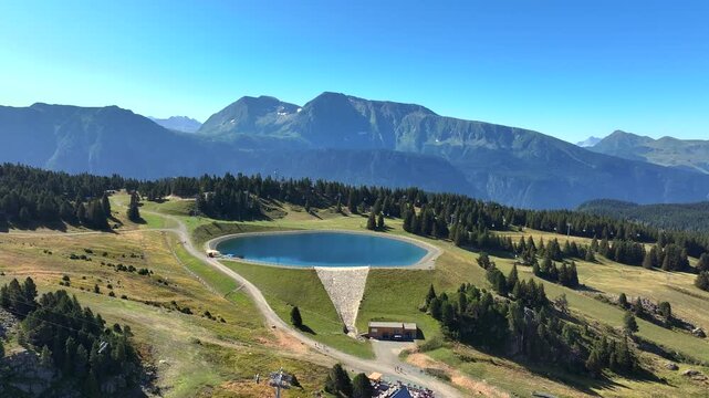 A breathtaking aerial view of the French Alps with the small alpine village of Chamrousse nestled among forested hills. The moving clouds and mountain ridges create a calm and cinematic summer 