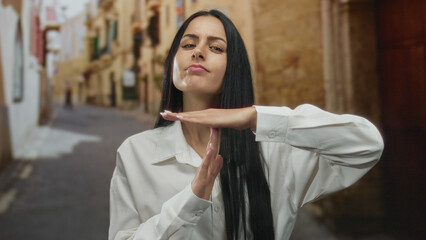 Naklejka premium Young hispanic woman making time-out gesture on old town street outdoors wearing white shirt with ancient buildings blurred in background capturing cultural essence and urban charm