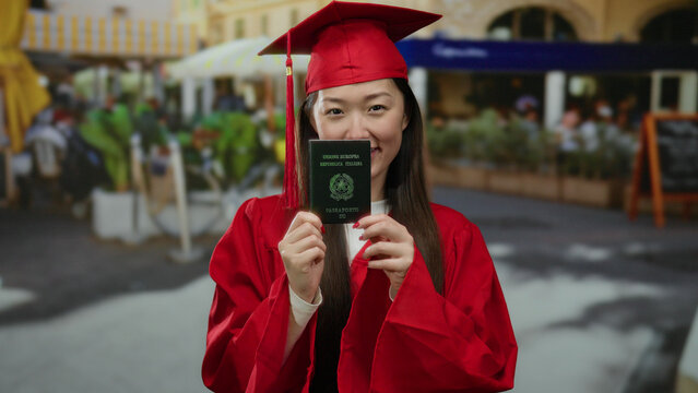 Fototapeta Woman in red graduation gown holding italian passport on a bustling city street cafe terrace showcasing cross-cultural achievement