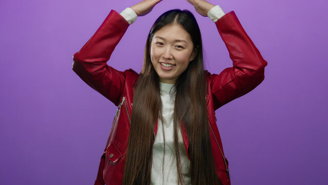 Woman dancing joyously in a red jacket against an isolated purple background, exuding happiness and energy with her raised arms and flowing hair.