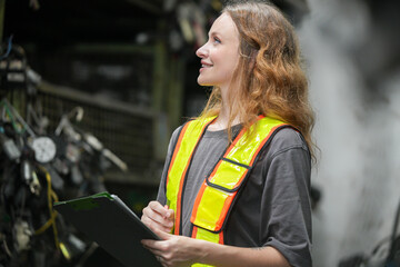 Female technician examine used car damaged engine block at scrapyard warehouse recycle scrap part....