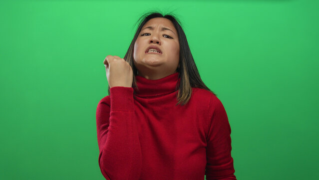 Young woman in red sweater making an expressive gesture with her hand against an isolated green background wall, conveying emotion and focus.