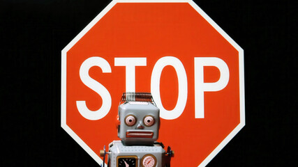 Vintage robot toy in front of big red stop sign. Retro sci-fi figure warns of technology limits and...