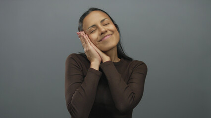 Woman gestures sleep against a grey background, embodying relaxation and tranquility, perfect for...