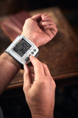 Man checking blood pressure and heart rate at home with a portable modern digital meter.
