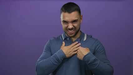 Young hispanic man in blue shirt clutch chest for heartattack in studio; pain resilience hope recovery.
