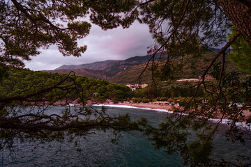 Idyllic coastal scenery with a secluded beach, lush vegetation, and mountain views captured at sunset.