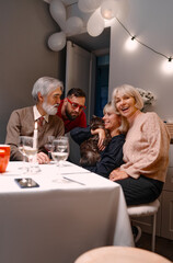 Naklejka premium A cozy gathering of family and friends enjoying each other's company indoors, sharing warm moments with a beloved pet cat. Decor and cheerful ambiance enhance the special occasion.