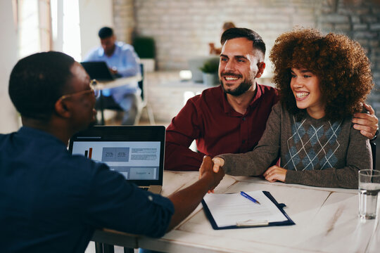 Excited couple celebrates a successful agreement as the Caucasian woman shakes hands enthusiastically with the African American advisor during a consultation - Powered by Adobe