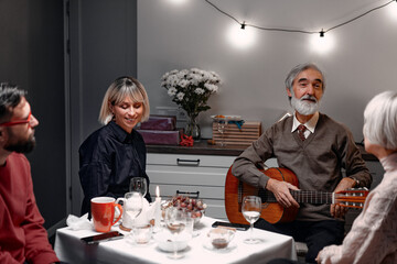 Cozy gathering of family sharing warm, relaxing dinner with beverages and live musical entertainment. Ambiance includes intimate lighting, friendly smiles, creating harmonious and joyous atmosphere.