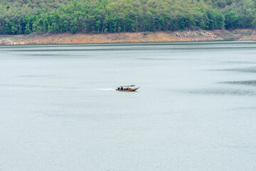 A long-tail boat carrying tourists with a blue canopy glides across a peaceful lake in Thailand, surrounded by calm water and natural scenery. Perfect image for travel and tourism concepts.