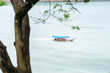 A long-tail boat carrying tourists with a blue canopy glides across a peaceful lake in Thailand, surrounded by calm water and natural scenery. Perfect image for travel and tourism concepts.