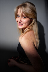 Naklejka premium A cheerful blonde woman with freckles smiles confidently, standing in natural light with shadow play creating an artistic effect. Her positive demeanor conveys a sense of joy and authenticity.