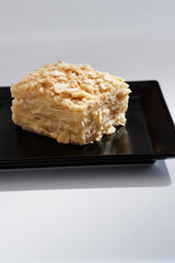 A creamy, layered dessert bar with a crumbly top sits on a sleek black plate. This image highlights texture and indulgence, ideal for dessert photography, bakery menus, and food styling.