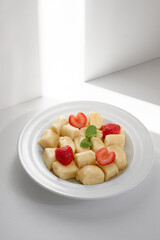 Clean, minimalist scene showing white plate filled with gnocchi, fresh strawberry halves, and mint garnish. Light and soft shadows emphasize freshness, creating inviting, healthy snack or dessert