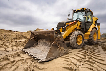 A powerful loader is shaping sand at a construction location while dark clouds gather in the sky, hinting at a change in the weather