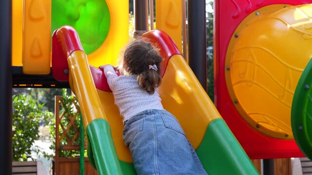 Little girl climbing up the colorful slide on a sunny playground