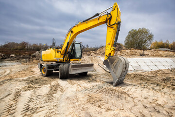 Obraz premium Bright yellow excavator digs into the earth at a construction site surrounded by trees, showcasing the hard work involved in building development