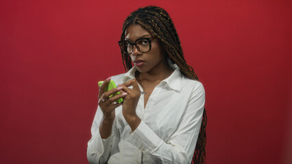 African american woman writing on green sticky notes with pen, hands poised over notes, posed against a red studio backdrop; concentration planning.