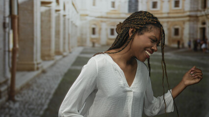 African american woman dancing and smiling on an old town street with braided hair and loose white blouse; joy freedom movement.
