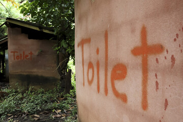 Rustic outdoor toilet and outhouse with hand painted orange sign on mud wall. simple rural hut showing basic sanitation, bleak scene reflecting poverty and necessity
