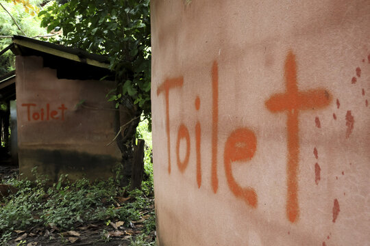 Rustic outdoor toilet and outhouse with hand painted orange sign on mud wall. simple rural hut showing basic sanitation, bleak scene reflecting poverty and necessity