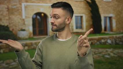 Young man in rustic mediterranean setting gestures with hand and finger against a stone house backdrop, conveying a point in an expressive manner, emphasizing communication style.